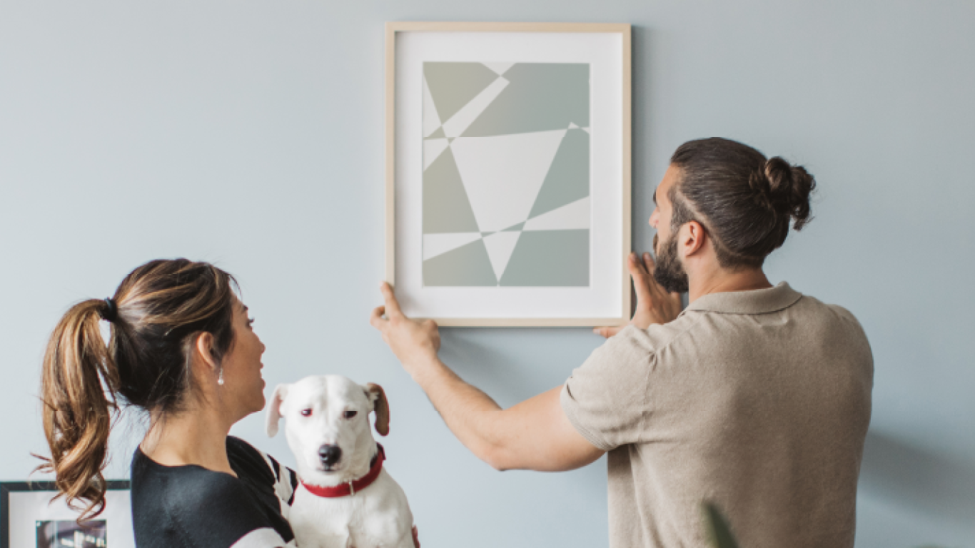 Una pareja con un perro colgando una foto en la pared