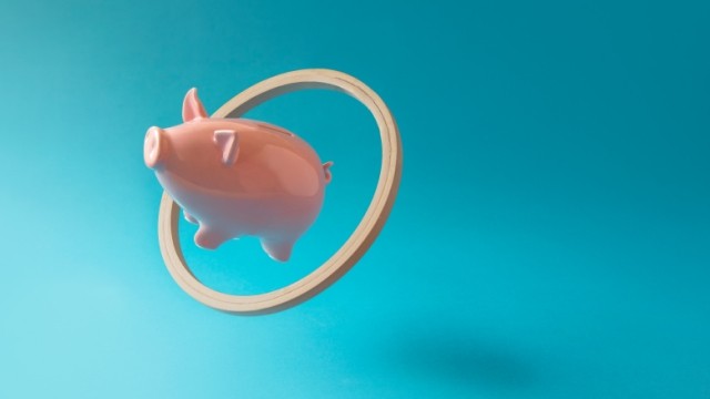 Pink piggy bank flying through hoop with ease on blue background.