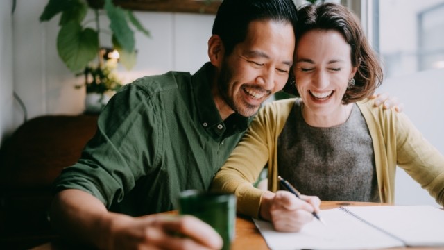 Two joyful partners reviewing finances at the kitchen table.