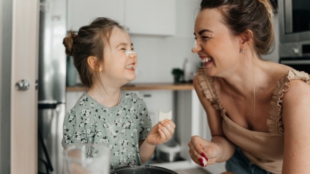 Mother and daughter baking in the kitchen, smiling and laughing together with flour on their noses.