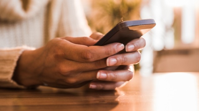 Two hands holding a cellphone on table.
