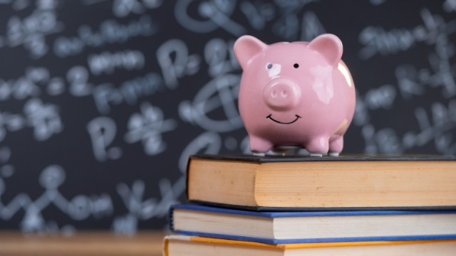 A pink piggy bank on top of a stack of three books with a school chalkboard in the background