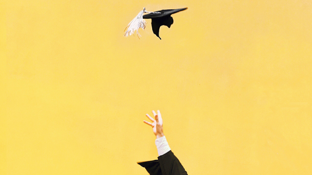 Hand throwing graduation cap into the air with a yellow background