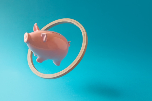 Pink piggy bank flying through hoop with ease on blue background.