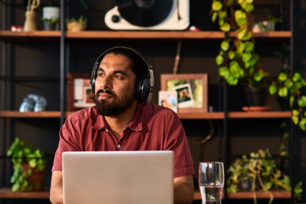 Gentleman sitting in office with laptop and headphones on looking off into the distance.