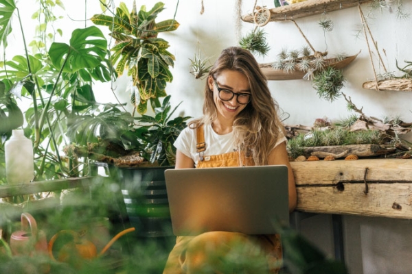 Woman plant shop business owner with glasses and hair down viewing laptop.