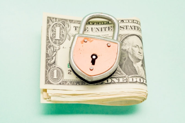 Dollar bills folded underneath copper lock on pale green background