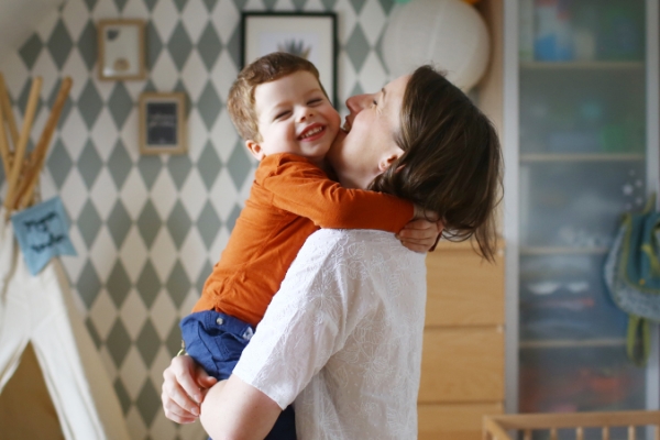 Mother and toddler hugging in home nursery with smiles.