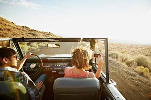 Couple driving on the open road in an old convertible car and taking photos.