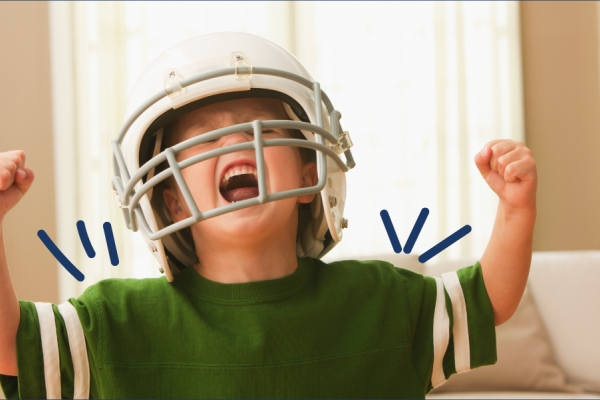 Little boy in an oversized football helmet shows his muscles and yells with excitement. 