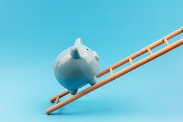 Light blue background with white porcelain piggybank climbing up a ladder.