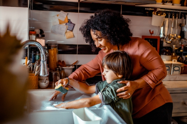 Mother with curly hair and son at home washing dishes in the sink
