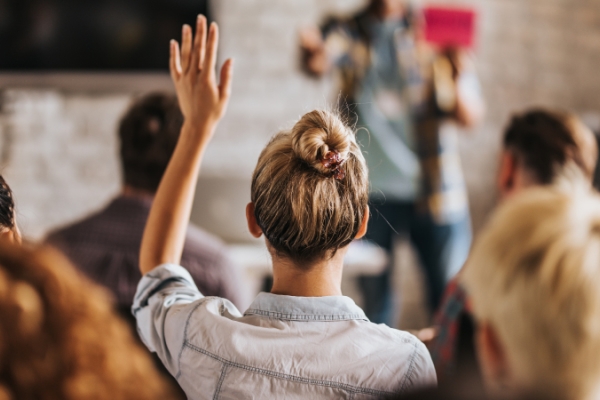 Girl with blonde hair in bun hairstyle raising hand.