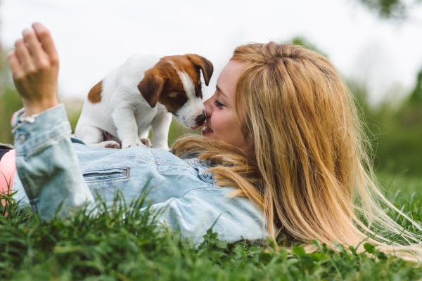 Woman laying in grass with puppy on top of her licking her face