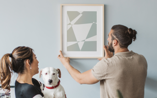Una pareja con un perro colgando una foto en la pared